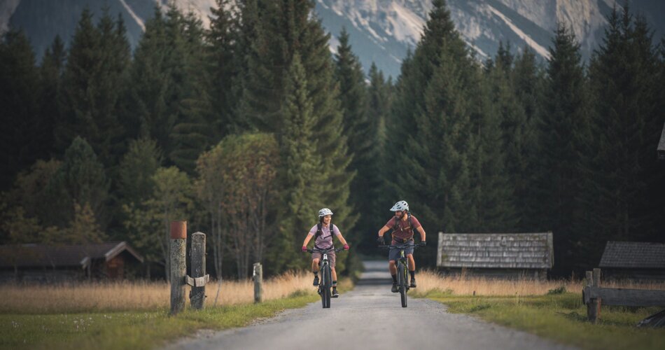 Two cyclists on a road, forest and mountains in the background | © Tiroler Zugspitz Arena/C. Jorda